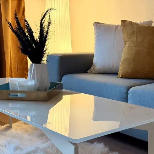 Ein stilvolles Wohnzimmer mit einem blauen Sofa und einem modernen Couchtisch. Der Tisch ist mit einer dekorativen Schale und einer Vase mit Pflanzen geschmückt.