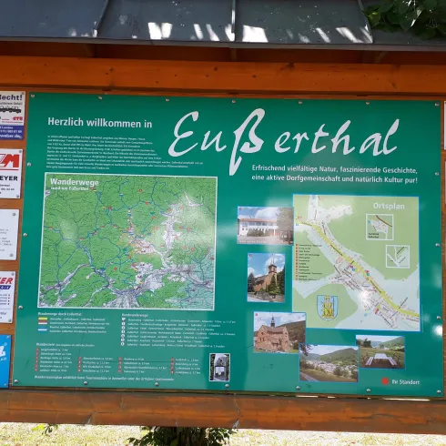 Eine Infotafel in Eusserthal mit einer Karte und Hinweisen zu Sehenswürdigkeiten. Die Tafel ist grün und steht unter einem Dach.
