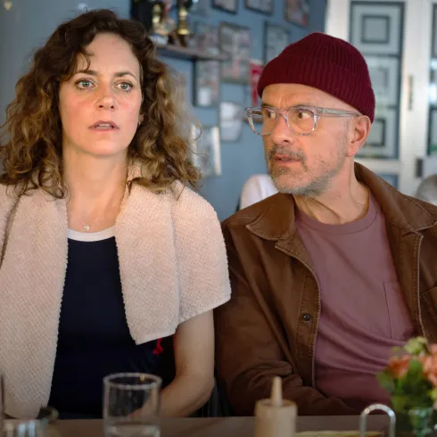 Ein Paar sitzt in einem Café und schaut aufmerksam. Die Frau sieht nachdenklich aus, während der Mann sie interessiert anblickt.
