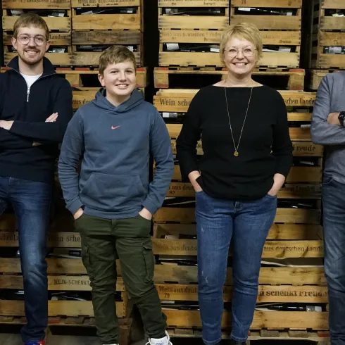 Eine Gruppe von vier Personen steht vor Holzregalen. Sie lächeln freundlich und wirken entspannt.