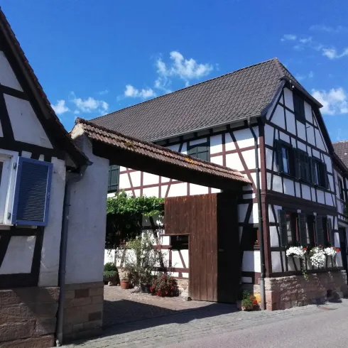Ein traditionelles Fachwerkhaus mit einem Eingang und blauen Himmel im Hintergrund. Die Umgebung ist ruhig und einladend.
