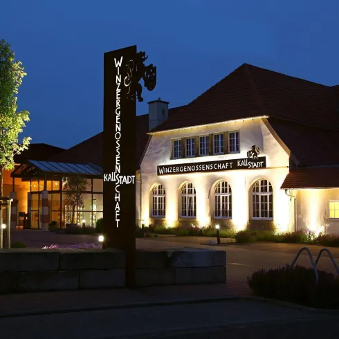 Das Gebäude der Winzergenossenschaft in Kallstadt vo Außen und am Abend, mit schöner Beleuchtung.