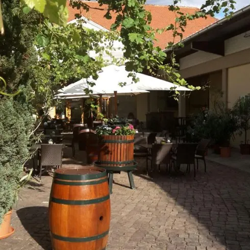 Ein Innenhof des Restaurants mit Holztischen und Sonnenschirmen. Die Weinreben verzieren den Innenhof.