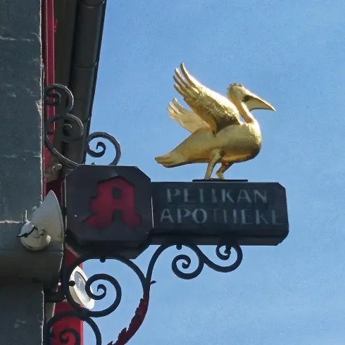 Ein goldenes Pelikan-Symbol auf einem Schild für eine Apotheke. Der Himmel ist klar und blau.