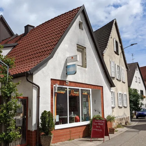 Ein charmantes Dorf mit traditionellen Häusern und roten Dächern. Die sonnige Straße vermittelt eine einladende Atmosphäre.