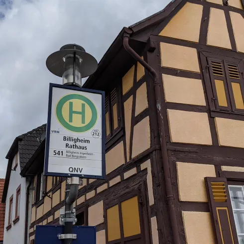 Eine Bushaltestelle an einem historischen Fachwerkhaus. Der Himmel ist teilweise bewölkt.