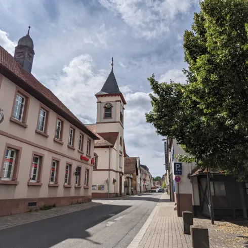 Eine ruhige Straße mit historischen Gebäuden und einer Kirche im Hintergrund. Die Atmosphäre ist entspannt und einladend.