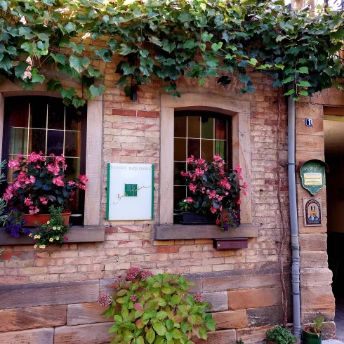 Ein charmantes Haus mit Ziegelsteinfassade und bunten Blumen in den Fenstern. Umgeben von grünen Pflanzen und einem einladenden Ambiente.