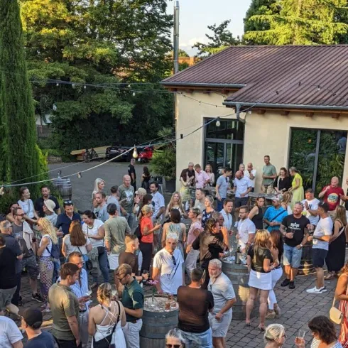 Eine große Menschenmenge versammelt sich im Freien, um gemeinsam zu feiern. Die Atmosphäre ist lebhaft und freundlich, mit einer schönen Umgebung.