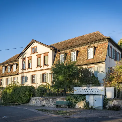 Ein großes, historisches Haus mit einem schönen Dach und vielen Fenstern. Es ist von Bäumen und einem Garten umgeben.