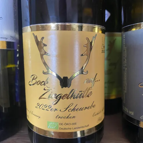 Ein Weinflasche mit einer goldenen Etikette, die den Jahrgang 2022 und die Rebsorte Scheurebe zeigt. Der Wein ist trocken und trägt ein elegantes Design mit Geweihsymbolen.