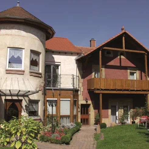 Ein charmantes Haus mit einem runden Turm und einem Balkon. Der Garten ist gepflegt und lädt zum Entspannen ein.