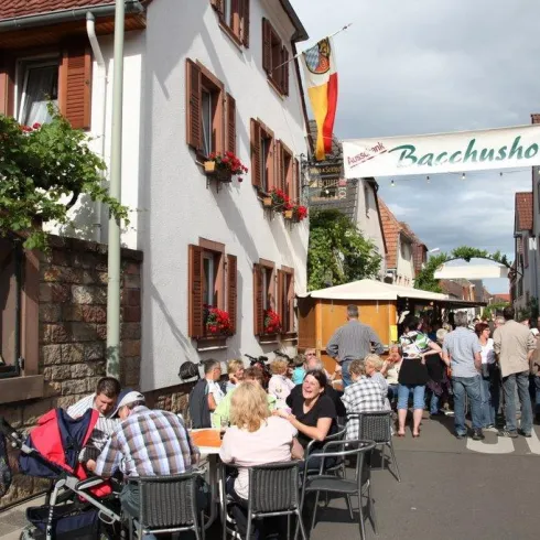 Eine belebte Straße mit Menschen, die an Tischen sitzen und essen. Im Hintergrund sieht man traditionelle Häuser und eine Fahne.