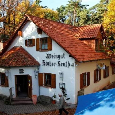 Ein malerisches Weingut mit einem traditionellen, rot gedeckten Dach. Die Umgebung ist von bunten Herbstbäumen umgeben.