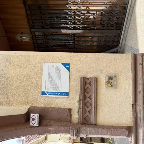 Ein Wandbereich mit einer Informationstafel und einer Eingangstür im Hintergrund. Die Umgebung wirkt freundlich und einladend.