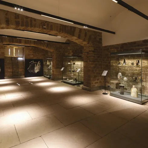 Ein Innenraum eines Museums mit Steinwänden und mehreren Vitrinen. In den Vitrinen sind verschiedene Ausstellungsstücke zu sehen.