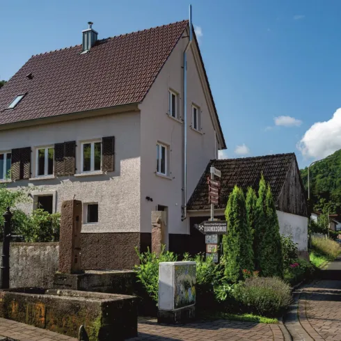 Ein charmantes, zweigeschossiges Haus mit einem roten Dach und Garten. Die Straße ist von grünen Bäumen und der Landschaft umgeben.