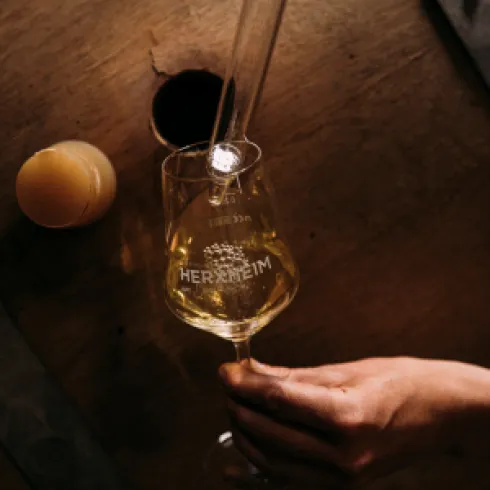 Ein Weinfass das geöffnet wurde und aus dem ein Glass Wein entnommen wird. Auf dem Foto wird ein Glass Wein befüllt.