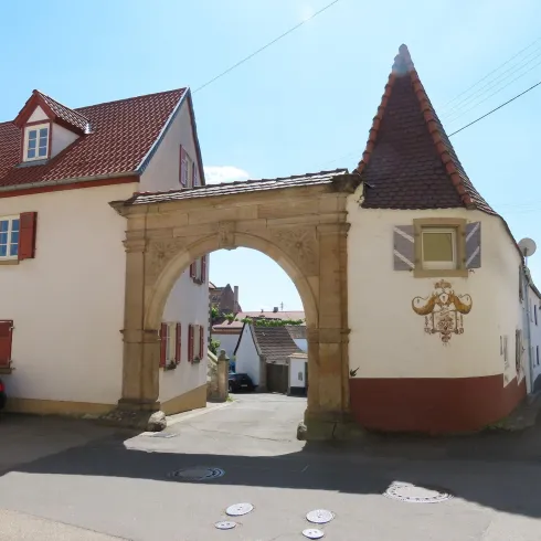 Ein Steintor zwischen zwei Häusern. Das Tor ist Rund und verschnörkelt. Durch das Tor geht eine Straße.