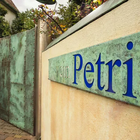Eine Steinmauer auf dem ein Schild mit dem Namen des Weinguts steht " Petri".