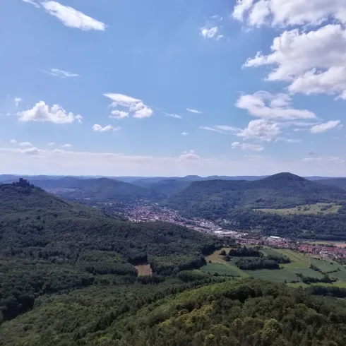 Eine weite Aussicht auf eine grüne Landschaft mit Hügeln und einem kleinen Dorf im Tal. Der Himmel ist klar und leicht bewölkt.