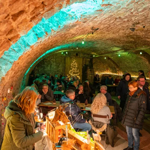 Eine gemütliche Kellerbar mit vielen Gästen. Die Wände sind aus Stein und mit festlicher Beleuchtung dekoriert.