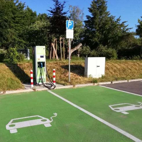 Eine Ladestation für Elektroautos steht auf einem Parkplatz. Die Stellplätze sind grün markiert und mit Symbolen für Elektrofahrzeuge versehen.