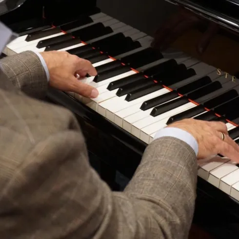 Ein Musiker spielt Klavier. Die Hände sind über den Tasten angeordnet und der Fokus liegt auf der Musik.