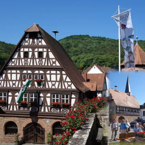 Eine traditionelle Fachwerkhaus mit blühenden Blumen im Vordergrund. Im Hintergrund sind grüne Hügel und weitere historische Gebäude zu sehen.