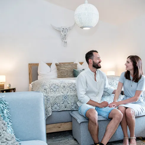 Zwei Personen sitzen am Bettrand in einem hellen, schön eingerichteten Hotelzimmer in der Pfalz.