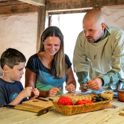 Zwei Erwachsene und ein Kind werkeln wie damals die Kelten im Keltendorf am Donnersberg mit traditionellem Werkzeug.