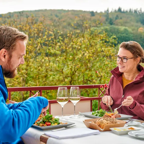 Zwei Personen sitzen auf der Terrasse des Verwöhnhotels Bastenhaus und genießen ein Essen mit Blick auf den Pfälzerwald.