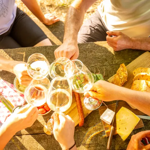 Menschen stoßen mit Weingläsern an einem Rastplatztisch mit Snacks an.