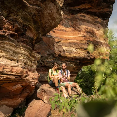 Ein Paar sitzt vor einer Sandsteinfelswand im Pfälzerwald und picknickt.