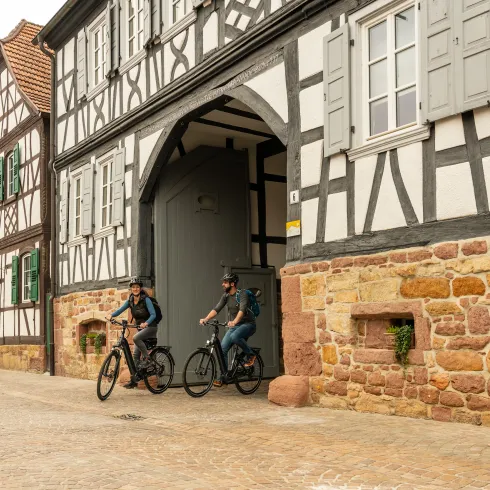 Zwei Prrsonen radeln entlang der Fachwerkhäuser von Steinweiler.