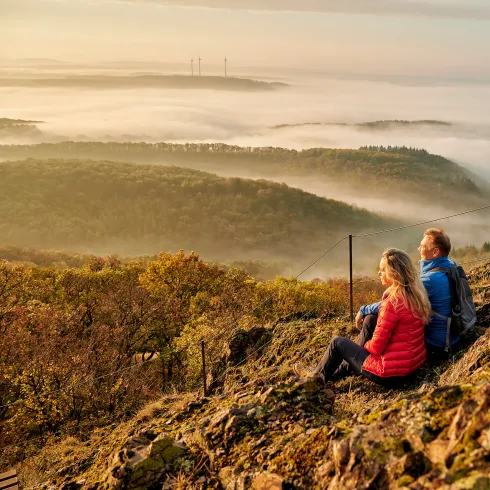 Zwei Personen betrachten den Ausblick über die Wälder und Hügel am Donnersberg.