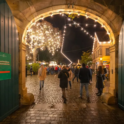 Die Weihnachtslichter des Deidesheimer Weihnachtsmarktes erleuchten die Straße, durch die Menschen schlendern.