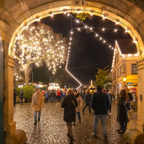 Besuchende des Deidesheimer Weihnachtsmarkt schlendern entlang der Buden durch das Winzerdorf.