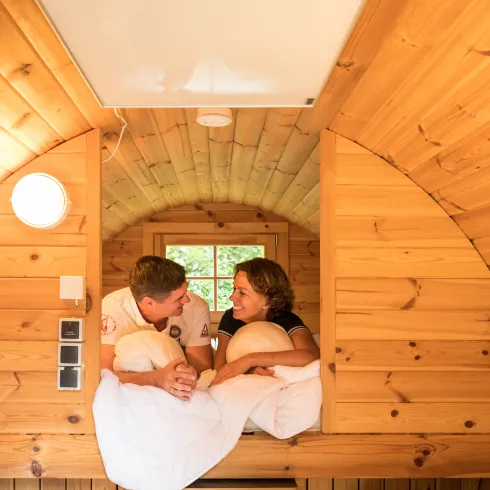 Zwei Personen liegen auf einem Bett in einer Glampinghütte aus Holz. 