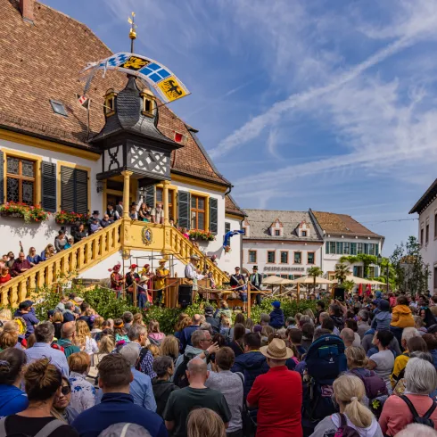 Menschen schauen bei der historischen Geißbockversteigerung in Deidesheim zu. 