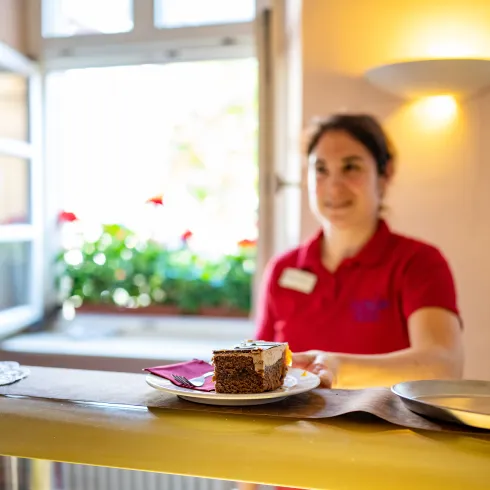 Eine Person steht hinter der Theke und überreicht Kuchen und Café. 
