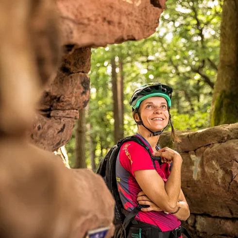 Eine Mountainbikerin steht vor dem Kellerfels im Pfälzerwald.