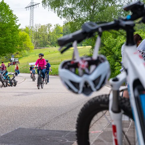 Ein Helm im Vordergrund und Personen die auf einem Weg radeln.