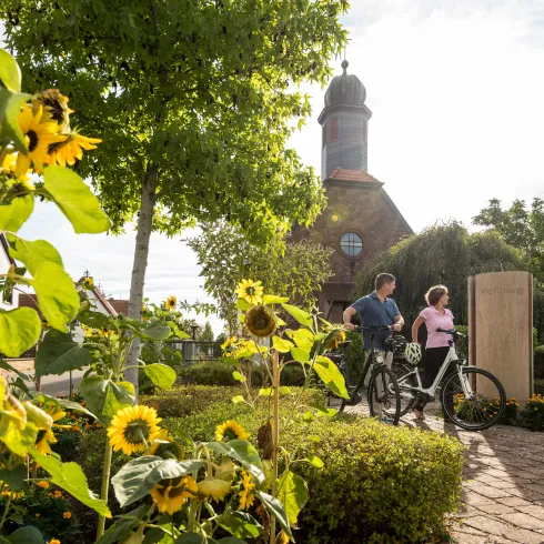 Zwei Personen laufen mit ihrem Rad durch Schwedelbach, vorbei an der Ortskirche.