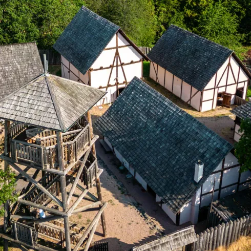 Das Keltendorf am Donnersberg mit rekonstruierten Holzhäusern und Palisaden, eingebettet in die hügelige Landschaft des Berglandes.