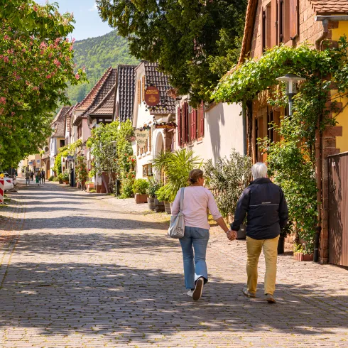 Ein Paar spaziert durch die Theresienstraße in Rhodt unter Rietburg. Eine Pflastersteinstraße mit alten Fachwerkhäusern.