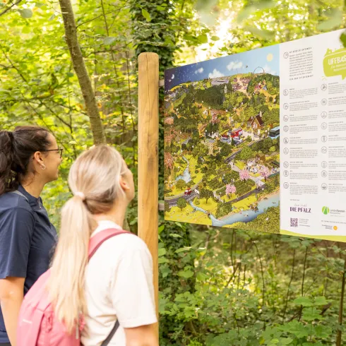  Zwei Personen schauen sich die Uffbasse-Infotafel mit Wimmelbild bei Offenbach an der Queich an.