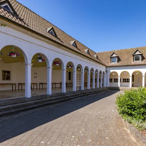 „Ein weißes Gebäude mit einer Terrasse aus Rundbögen an der Fassade.