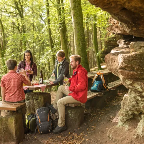 Eine Familie macht am Rastplatz vor einem Sandsteinfelsen im Pfälzerwald rast.