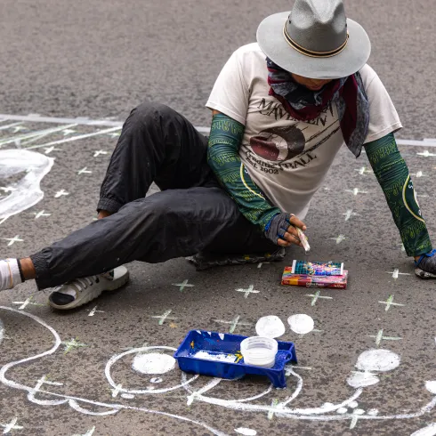 Eine Straßenkünstlerin zeichnet mit Kreidestiften ein Kunstwerk auf den Boden.